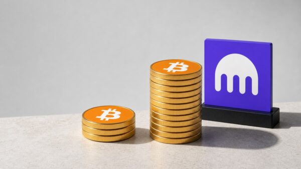 Auf einer hellen Steinfläche liegt links ein Stapel aus drei Goldmünzen mit dem Bitcoin-Zeichen, rechts daneben ein dreimal so hoher Stapel derselben Münzen; dahinter steht ein violettes Schild mit dem weißen Kraken-Zeichen.
