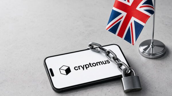Ein Smartphone mit dem Cryptomus-Logo auf dem Display liegt unter einer Stahlkette mit Vorhängeschloss, links steht eine britische Tischflagge.