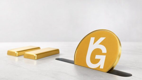 Eine große goldene Münze mit weißem K-G-Zeichen steckt halb in einem Schlitz in einer weißen Steinfläche, dahinter liegen zwei Goldbarren.